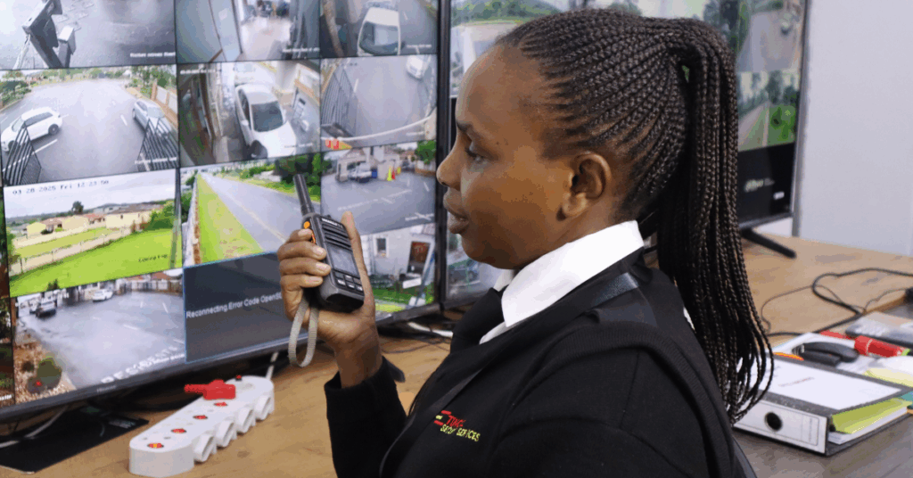 Female security officer monitoring multiple CCTV camera feeds and communicating with a two-way radio at a control room desk