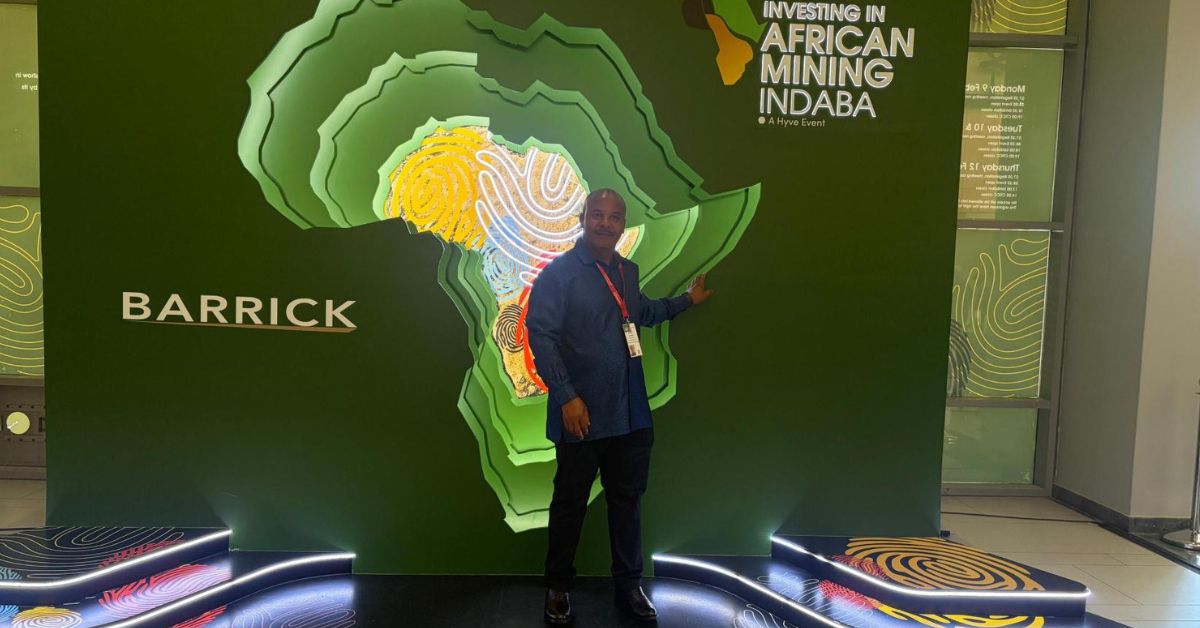 Man standing at the Investing in African Mining Indaba event display in front of an Africa-themed backdrop with Barrick branding.